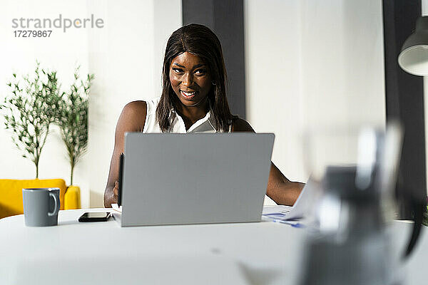 Lächelnde Geschäftsfrau  die an einem Laptop arbeitet  während sie am Schreibtisch im Büro sitzt
