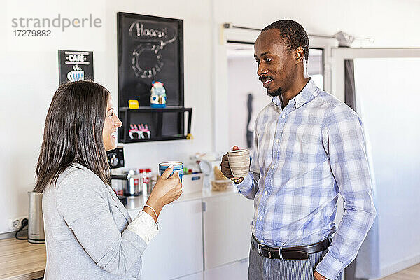 Lächelnde männliche und weibliche Unternehmer unterhalten sich bei einem Kaffee in der Pause im Büro