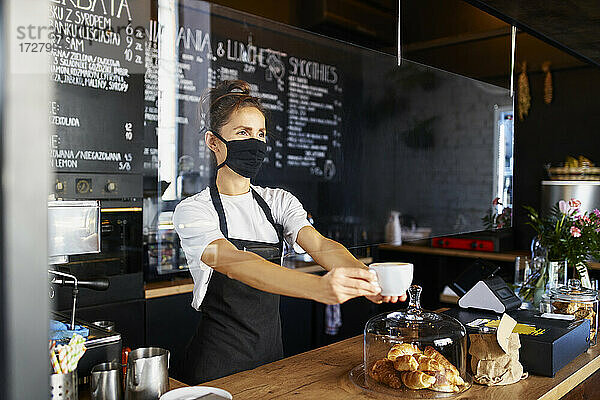 Kellnerin mit Gesichtsschutzmaske bei der Kaffeeausgabe in einem Cafe