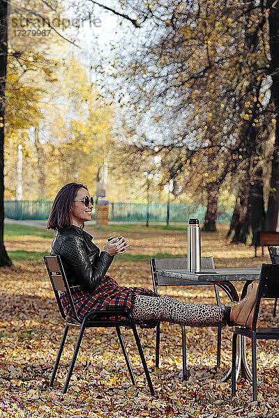 Mittlere erwachsene Frau trinkt Kaffee  während sie in einem öffentlichen Park sitzt