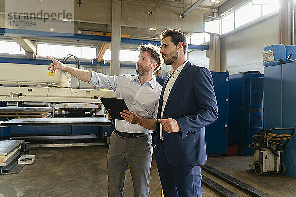 Geschäftsmann hält digitales Tablet bei der Arbeit  während er neben einem Geschäftsmann in einer Fabrik steht