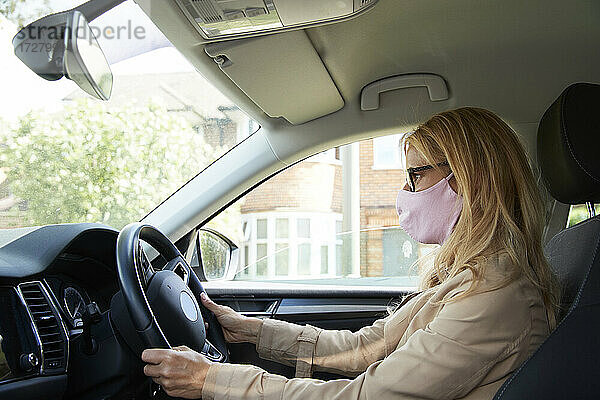 Ältere Frau mit Gesichtsschutzmaske beim Autofahren
