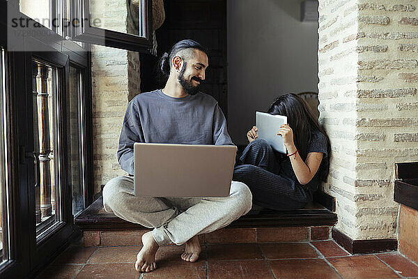 Lächelnder Vater betrachtet seine Tochter  die ihr Gesicht mit einem digitalen Tablet zu Hause versteckt