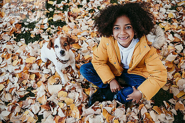 Lächelndes Mädchen sitzt mit Hund auf einem gefallenen Blatt im Park