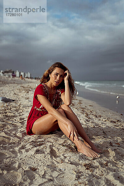 Nachdenkliche junge Frau sitzt am Strand