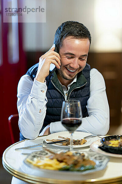 Junger Mann spricht am Esstisch eines Restaurants mit seinem Smartphone
