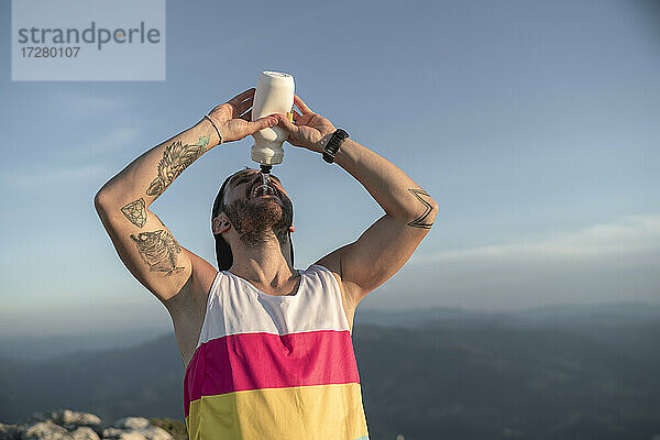Sportler trinkt Wasser  während er auf einem Berg gegen den klaren Himmel steht