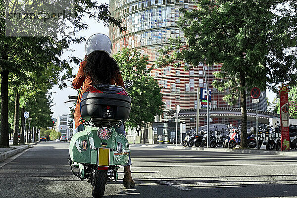 Junge Frau fährt Motorroller in der Stadt an einem sonnigen Tag