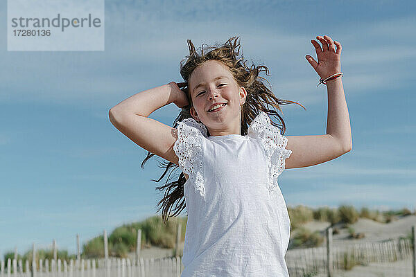 Mädchen mit Hand im Haar am Strand stehend an einem sonnigen Tag