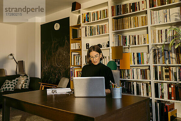 Freiberuflerin arbeitet an einem Laptop  der zu Hause am Bücherregal steht