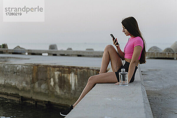 Frau benutzt Mobiltelefon  während sie auf einer Stützmauer sitzt