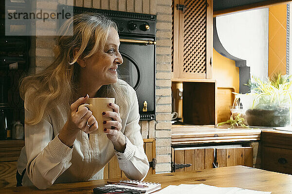 Lächelnde Frau  die Kaffee trinkt und sich zu Hause auf die Kücheninsel stützt