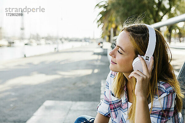 Junge Frau hört Musik über Kopfhörer auf einem Fußweg an einem sonnigen Tag