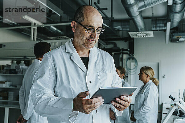Wissenschaftler arbeitet an einem digitalen Tablet  während er mit einem Kollegen im Hintergrund im Labor steht
