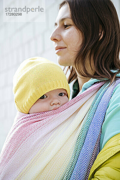 Mutter hält ihr in eine Decke eingewickeltes Baby und schaut an einem sonnigen Tag weg