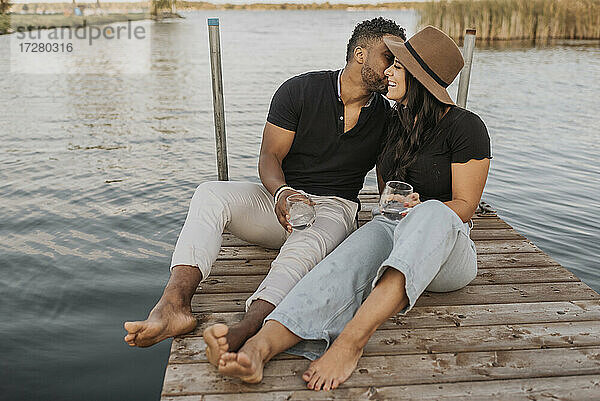 Freund küsst Freundin  während er auf einem Steg am See sitzt