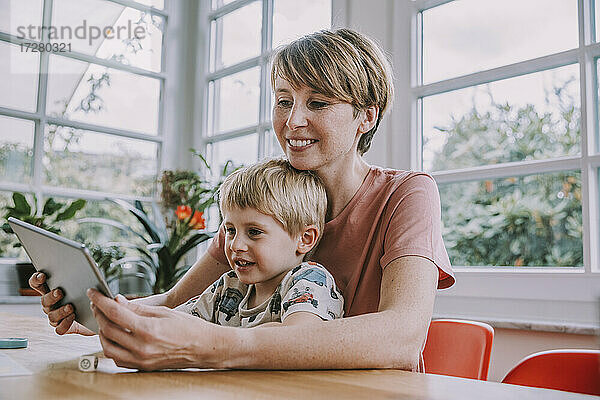 Mutter benutzt digitales Tablet mit ihrem Sohn  während sie zu Hause sitzt