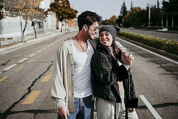 Lächelnde Frau hält Hände mit männlichem Partner  während sie auf der Straße in der Stadt steht