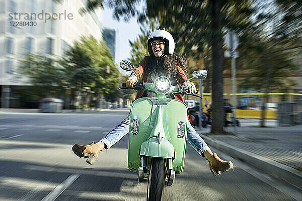Fröhliche Frau fährt Motorroller auf der Straße in der Stadt