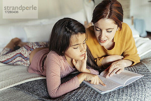 Mädchen und Frau lesen ein Buch  während sie zu Hause auf dem Bett liegen