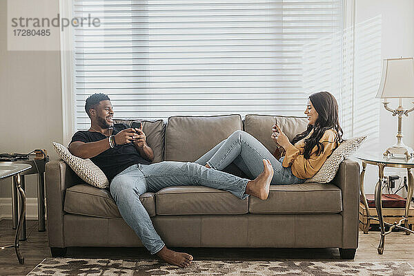 Ein Paar benutzt ein Mobiltelefon  während es zu Hause auf dem Sofa sitzt