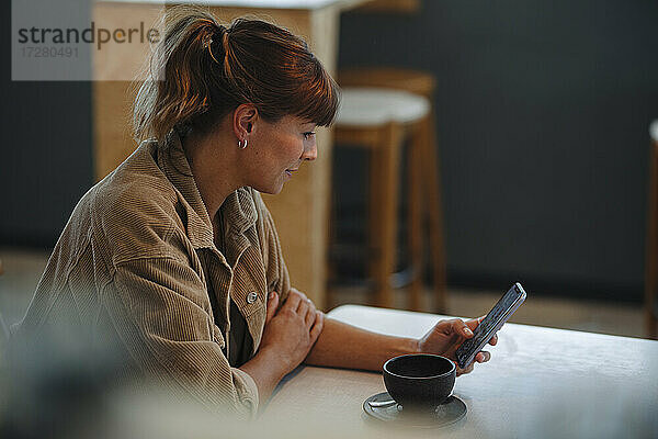 Weiblicher Besitzer Textnachrichten auf Smartphone sitzend im Café