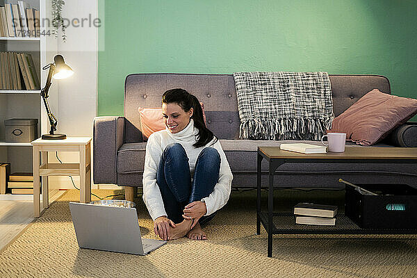 Mittlere erwachsene Frau  die einen Laptop benutzt  während sie zu Hause auf dem Boden sitzt