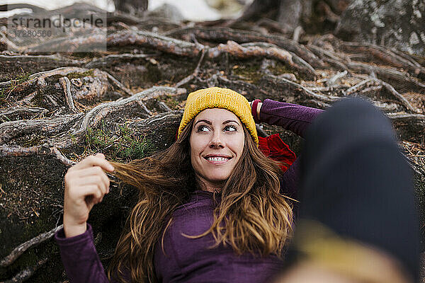 Lächelnde Frau  die wegschaut  während sie auf Baumwurzeln im Wald bei La Pedriza  Madrid  Spanien  liegt