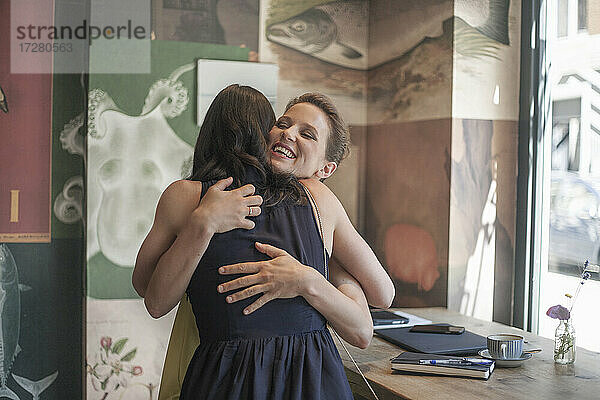 Lächelnde junge Geschäftsfrau  die ihre Freundin in einem Café umarmt
