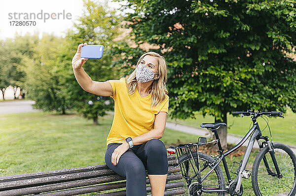 Frau macht Selfie mit Gesichtsschutzmaske auf einer Bank in der Stadt