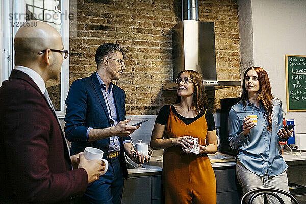 Männliche und weibliche Kollegen diskutieren bei einem Kaffee in der Büroküche