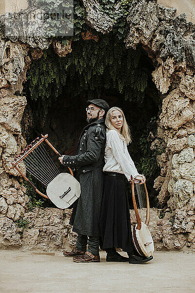 Frau mit männlichem Partner  der ein Lyra-Musikinstrument gegen ein Bauwerk hält