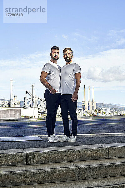Selbstbewusstes schwules Paar steht auf einer Brücke gegen den Himmel