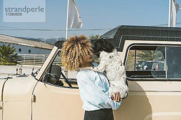 Junge blonde Afro-Frau mit Hund an einem alten Geländewagen an einem sonnigen Tag