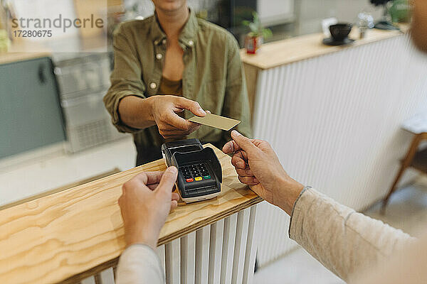 Mittelteil einer Unternehmerin  die einem Kunden an der Kasse eines Cafés eine Kreditkarte gibt
