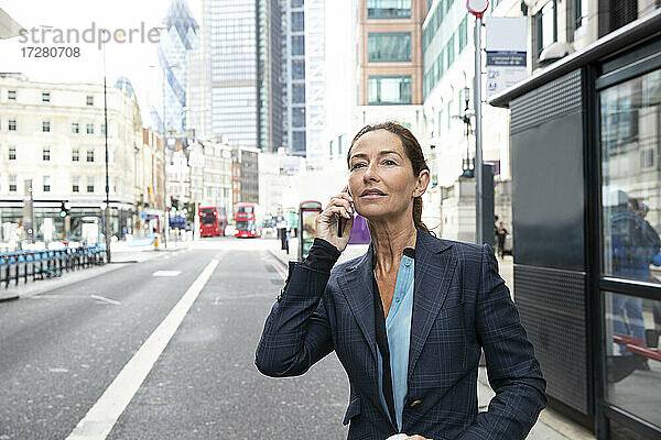 Frau in Geschäftskleidung  die auf einer Straße in der Stadt steht und mit einem Mobiltelefon spricht