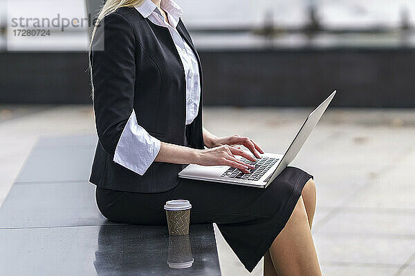 Geschäftsfrau arbeitet an einem Laptop  während sie auf einer Bank im Freien sitzt