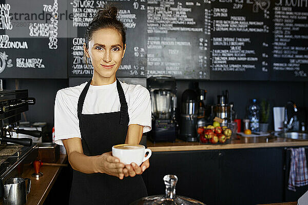Porträt einer lächelnden Kellnerin  die in einem Café Kaffee ausschenkt