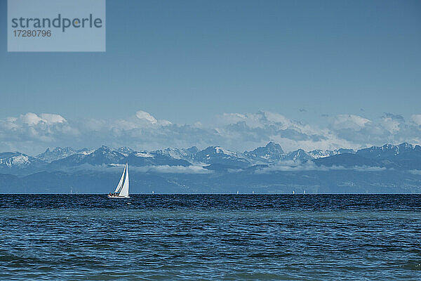 Einsames Segelboot auf dem blauen Wasser des Bodensees mit den Alpen im Hintergrund