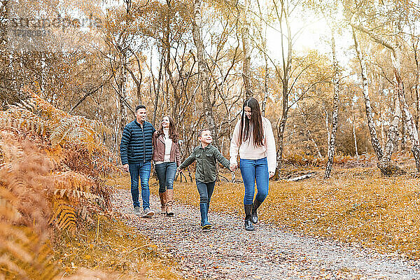 Familie hält sich an den Händen und geht im Herbst im Park spazieren