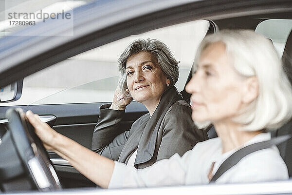 Geschäftsfrau lächelt  während sie neben einer Kollegin sitzt  die in der Stadt Auto fährt