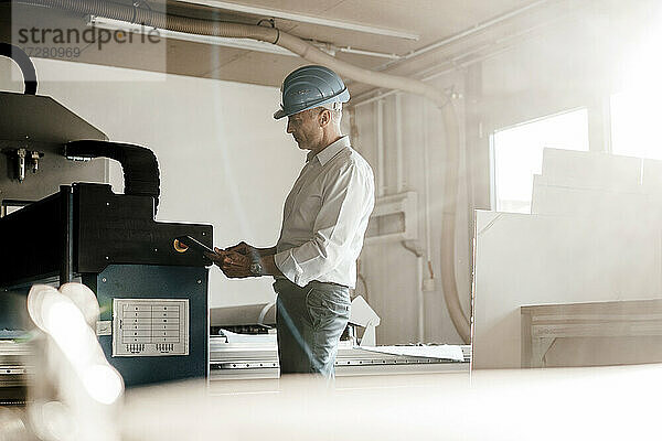 Ingenieur  der ein digitales Tablet benutzt  während er an einer Produktionsanlage in einer Fabrik steht