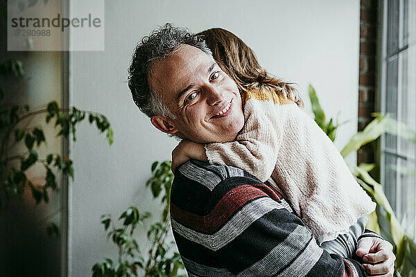 Vater lächelt  während er seine Tochter zu Hause in den Armen hält