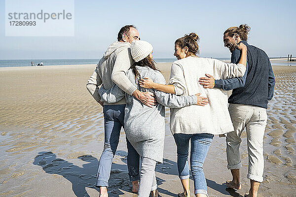 Familie mit Armen umeinander am Strand spazieren