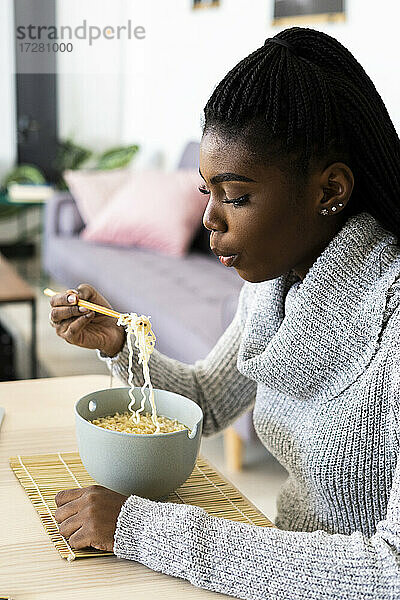 Frau isst Nudeln  während sie zu Hause sitzt