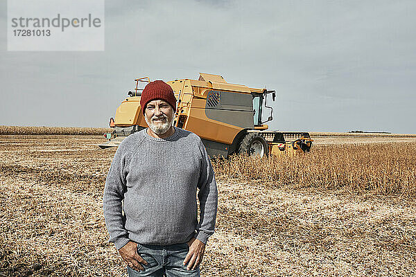 Lächelnder Landwirt  der vor einem Traktor steht  der auf einem Bauernhof erntet