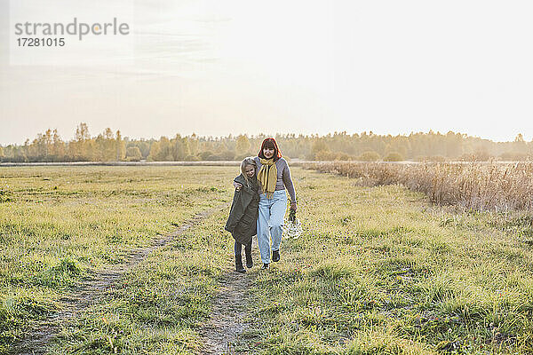 Ältere Frau geht mit ihrer Enkelin an einem sonnigen Tag auf einem Feld spazieren