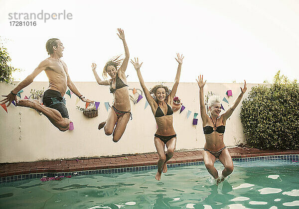 Unbekümmerte Freunde springen zusammen in den Pool gegen den Himmel bei Sonnenuntergang