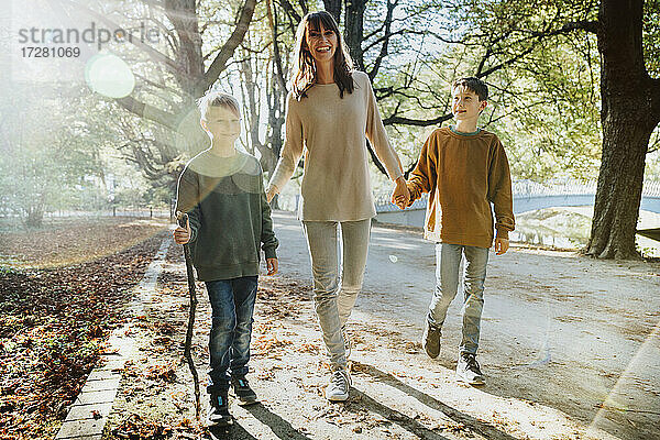 Glückliche Mutter und Söhne gehen im öffentlichen Park an einem sonnigen Tag spazieren