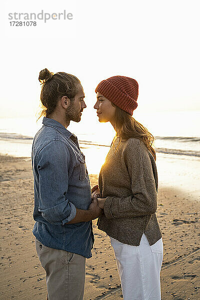 Romantisches junges Paar  das sich bei Sonnenuntergang am Ufer stehend ansieht